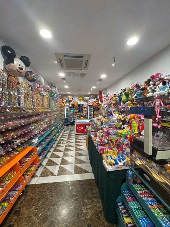 Interior de tienda de dulces con estantes de dulces, globos y peluches.