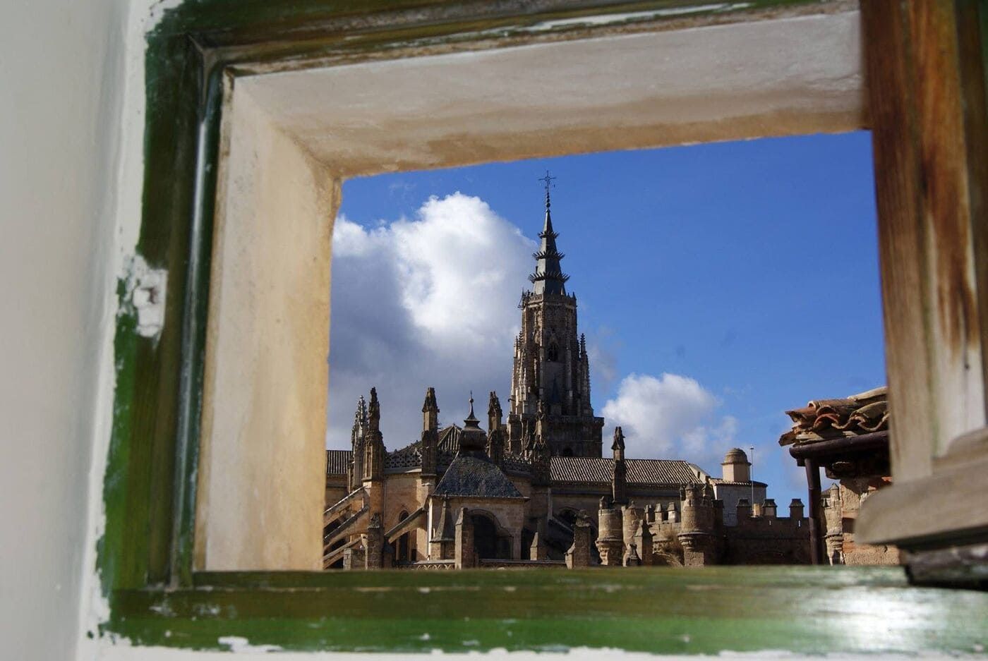 Catedral vista a través de una ventana con marco verde contra un cielo azul con nubes.
