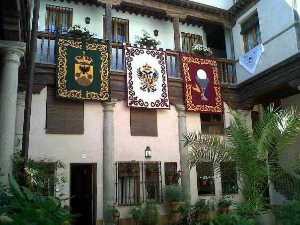 Patio con pancartas colgando de un balcón de madera. Columnas y ventanas enmarcan la escena.
