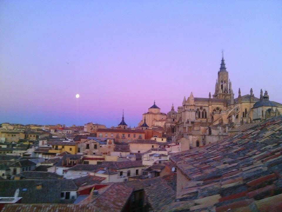 Vista desde la azotea de Toledo, España, al anochecer, con la catedral recortada contra un cielo lavanda y naranja. Luna visible.
