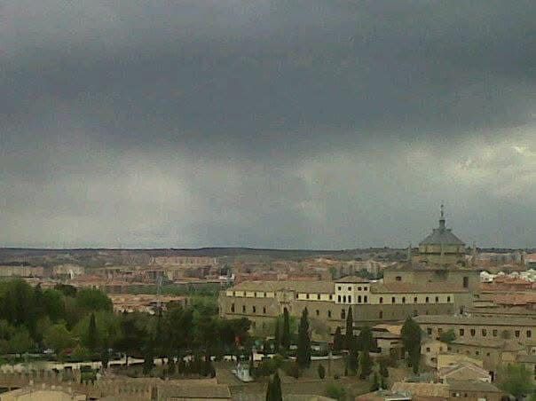 Paisaje urbano bajo un cielo oscuro y nublado. Edificios con tejados anaranjados, árboles y una estructura abovedada.