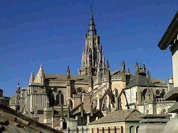 Catedral gótica con una alta aguja contra un cielo azul claro. El tejado es visible en primer plano.