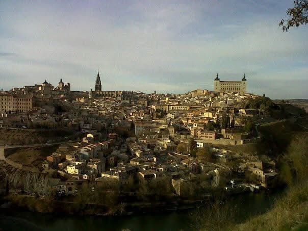 Toledo, España, paisaje urbano en una colina con una catedral y un castillo, visto desde el otro lado de un río, en un día nublado.