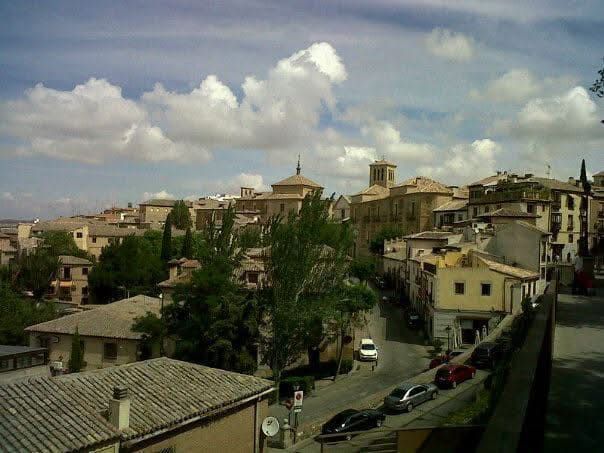 Paisaje urbano con edificios de piedra, calles y cielo nublado.