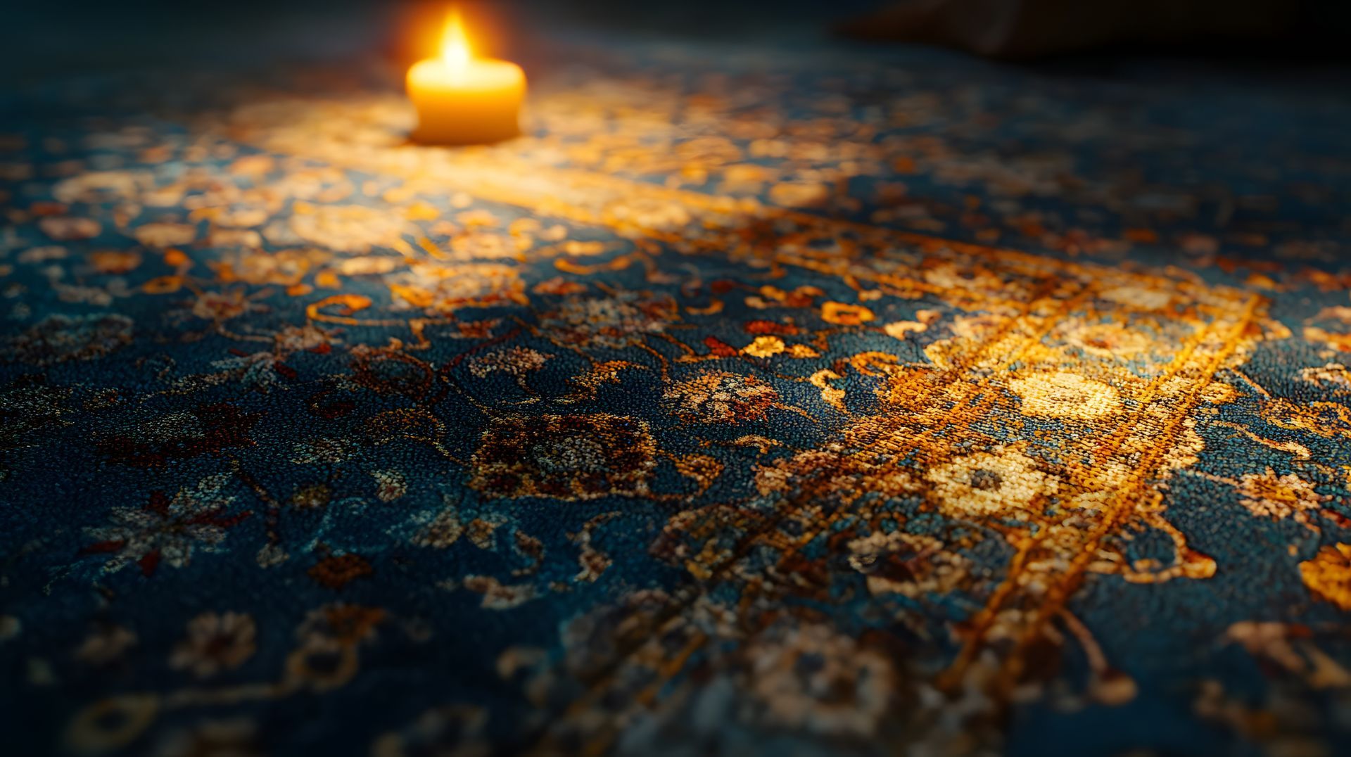 Une bougie allumée projette une lueur chaleureuse sur un tapis aux motifs bleus et or finement travaillés.
