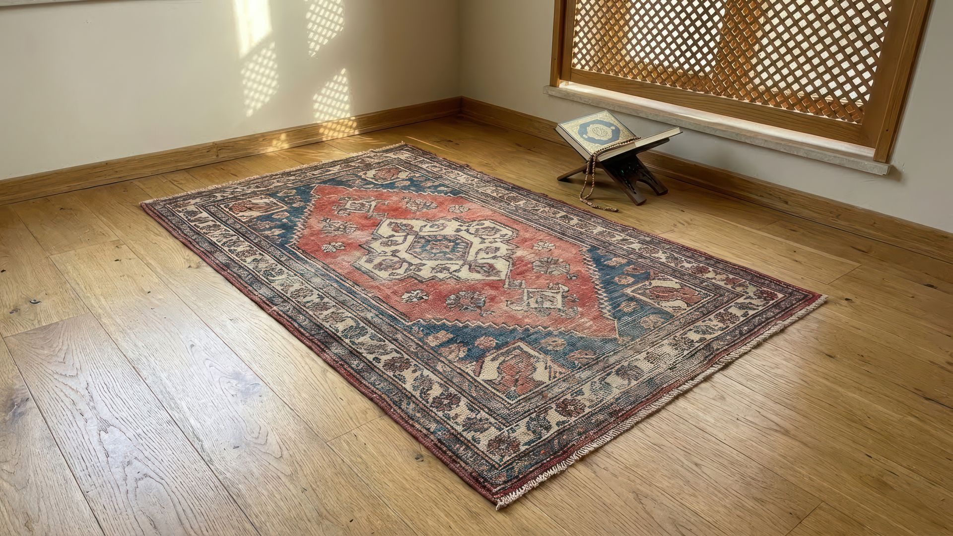 Un tapis ancien à motif central rouge et bleu est posé sur un parquet près d'une fenêtre à croisillons.