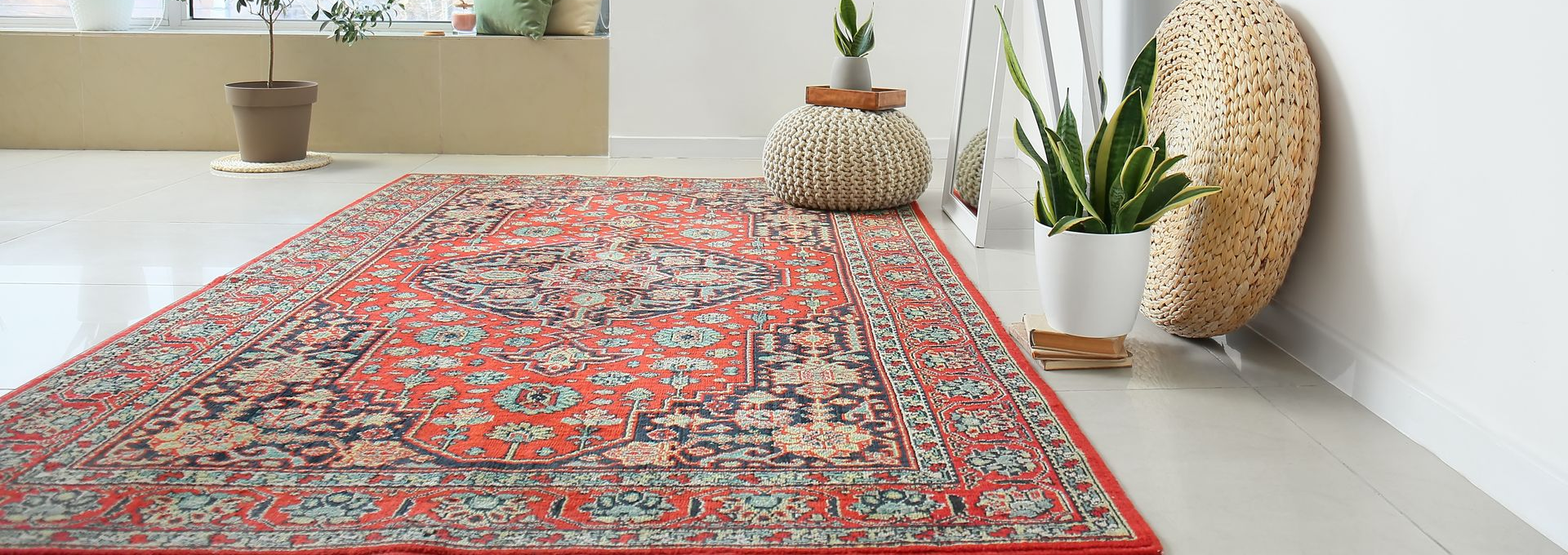 Tapis persan rouge sur un sol blanc, avec des plantes et un élément décoratif tissé.