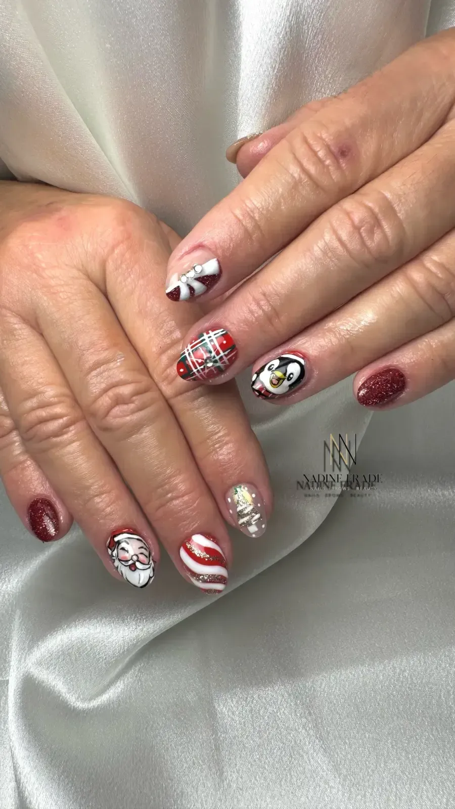 Manos con arte de uñas con temática navideña; diseños rojos, blancos y dorados sobre un fondo sedoso.