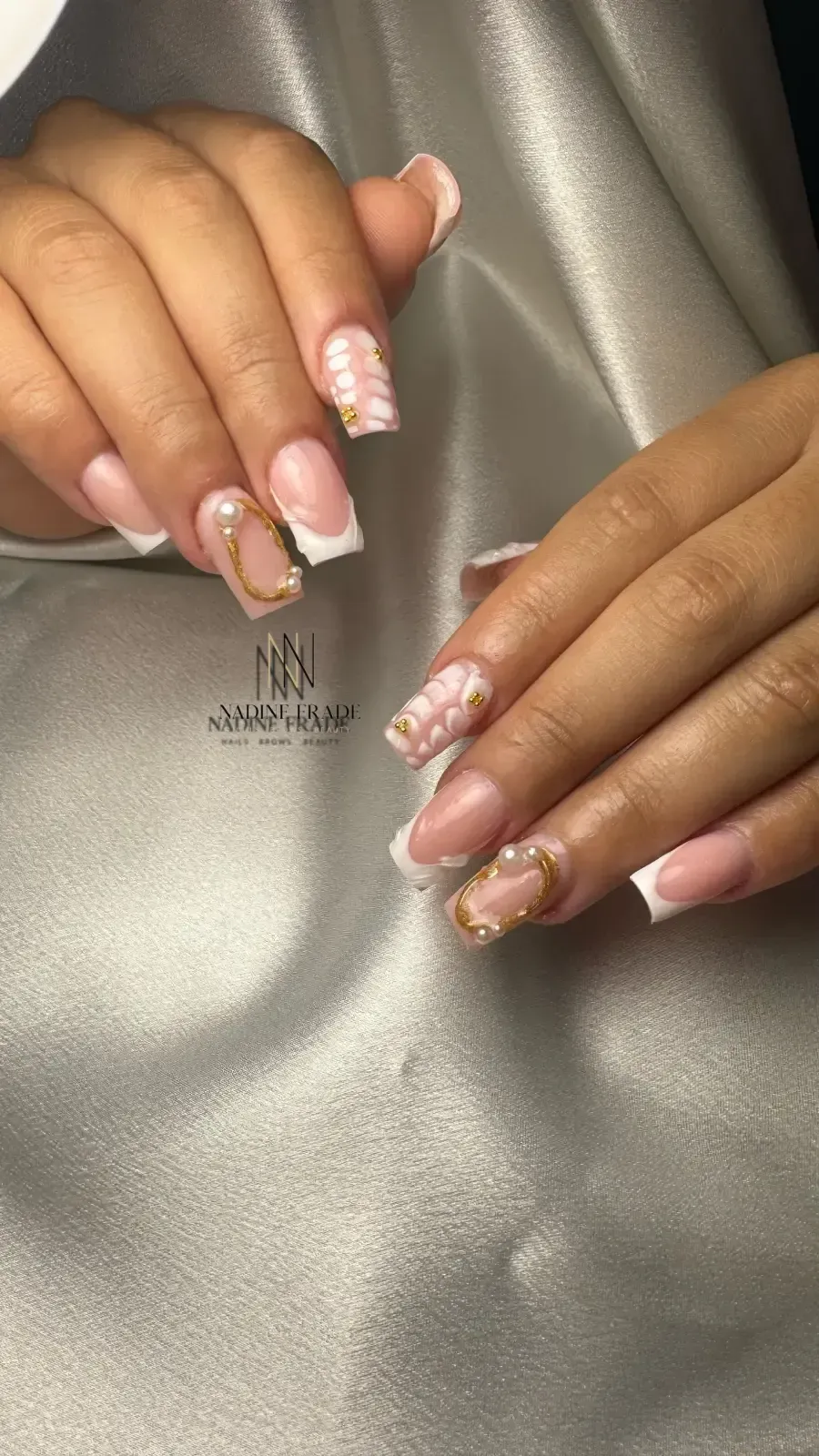 Manos con uñas cuadradas en estilo manicura francesa, algunas con adornos dorados.