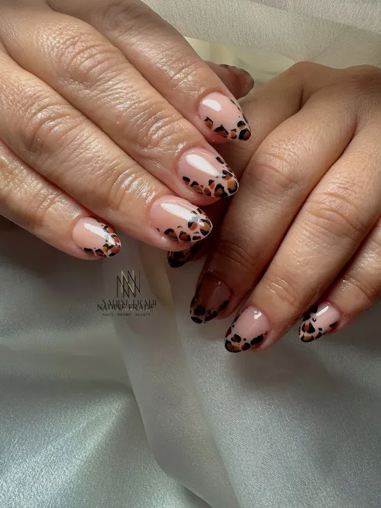 Manos con uñas en forma de almendra que presentan una base transparente con puntas con estampado de leopardo.
