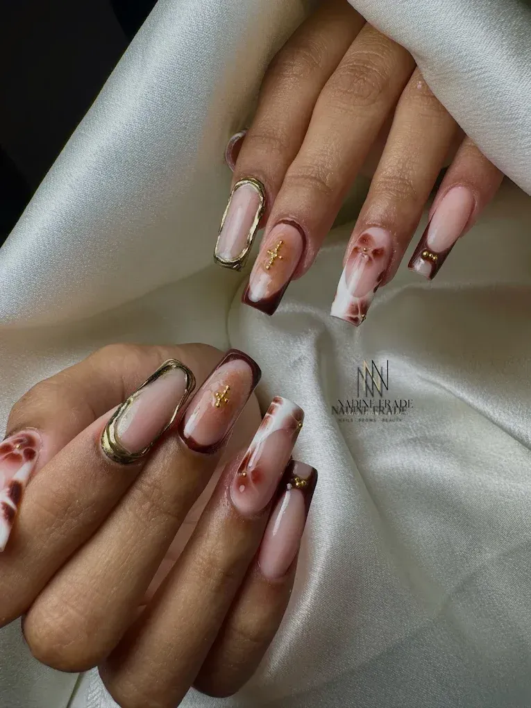 Uñas cuidadas con detalles dorados y acentos granates, sobre un fondo de seda blanca.