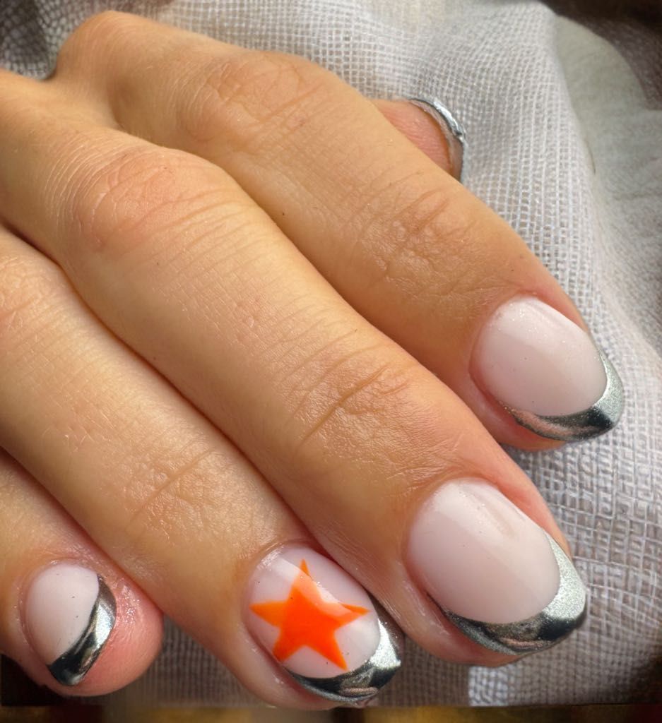 Mano con uñas ovaladas, algunas con puntas plateadas, una con diseño de estrella naranja.
