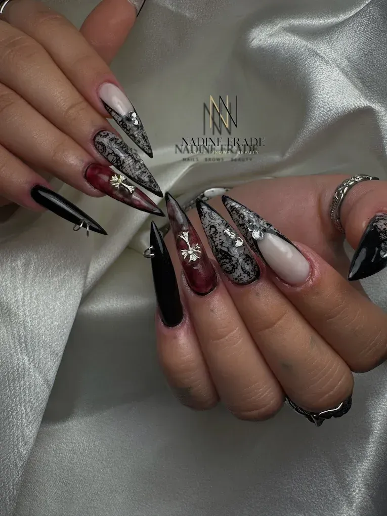 Primer plano de uñas cuidadas. Uñas largas, negras, rojas y nude, con diseños intrincados y adornos sobre un fondo sedoso.