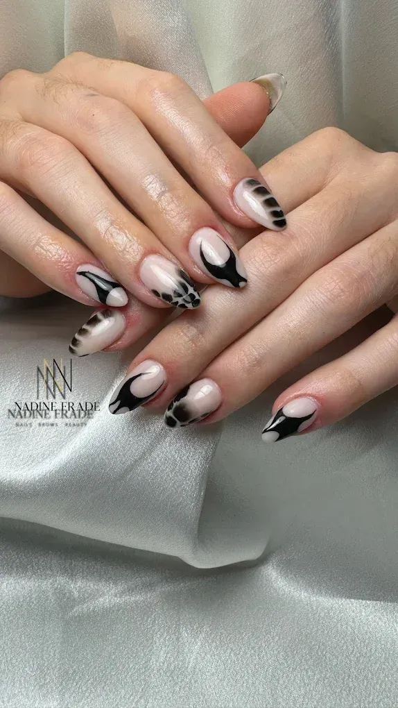 Manos con uñas largas y almendradas. Uñas color nude con diseños abstractos negros sobre fondo blanco.