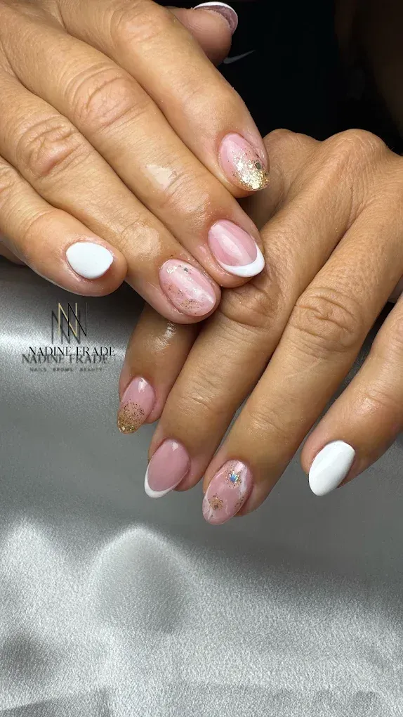 Manos con uñas de forma ovalada, con puntas blancas, francesas y acentos de brillo dorado.