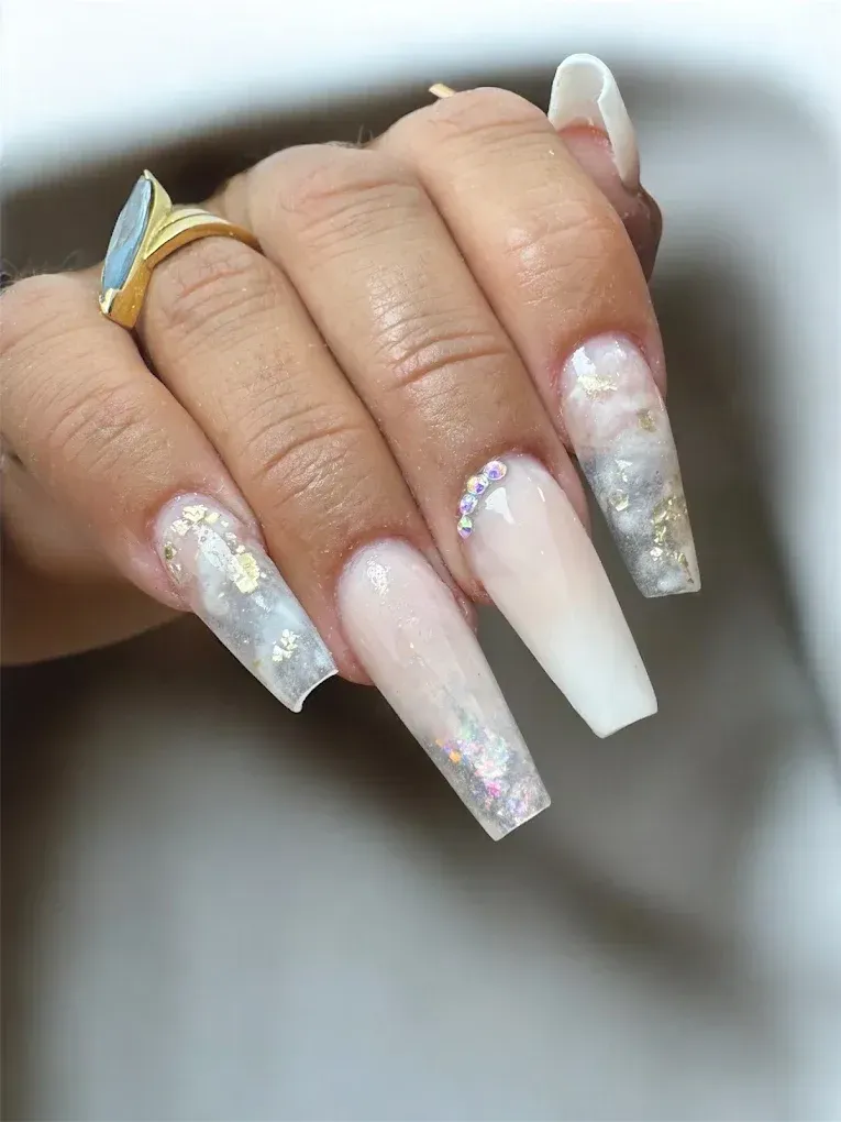 Mano con uñas largas en forma de ataúd. Diseños de perlas y brillantina, con un anillo dorado en el dedo.