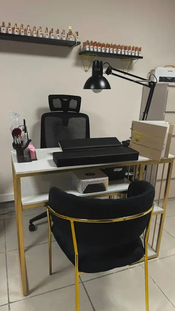 Estación de decoración de uñas con escritorio, lámpara, silla y estantes que contienen botellas de esmalte de uñas.