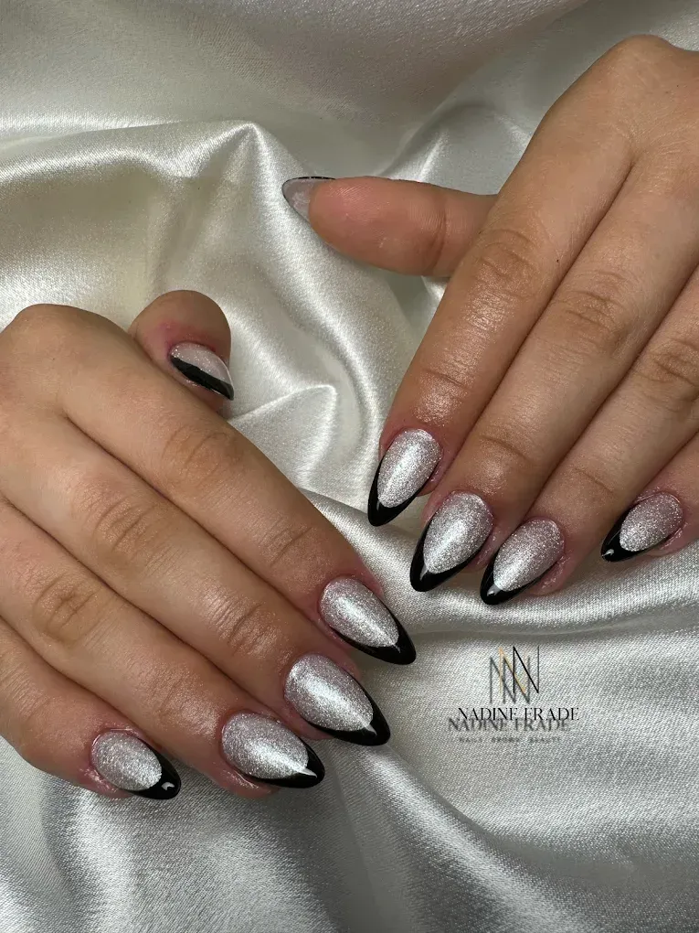 Manos con uñas con brillo plateado y puntas francesas negras apoyadas sobre tela de satén blanco.