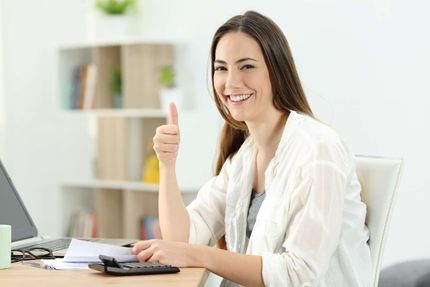 Una mujer está sentada en un escritorio haciendo un gesto de aprobación con el pulgar hacia arriba.