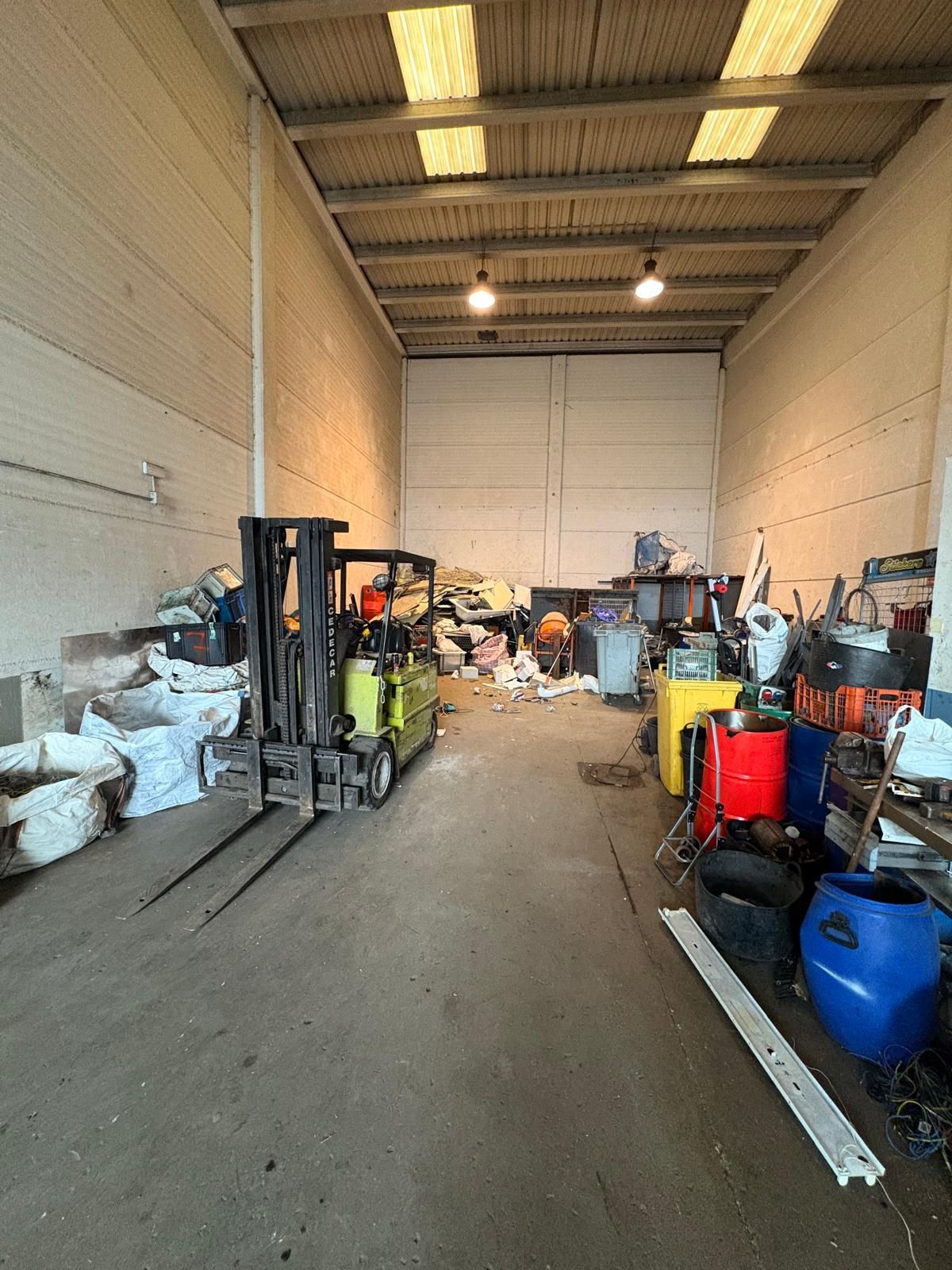 Vista interior de un almacén con una carretilla elevadora, varios artículos y un techo de metal.