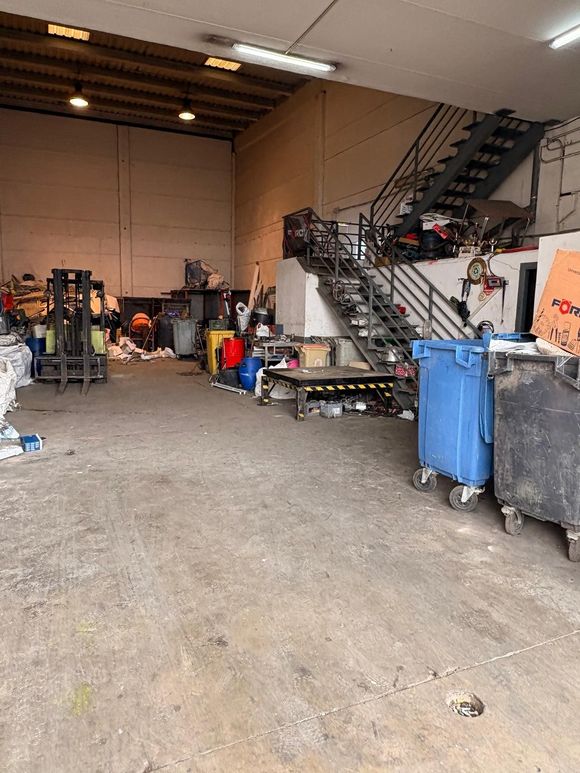 Interior de un espacio industrial desordenado con escaleras, contenedores y varios equipos.