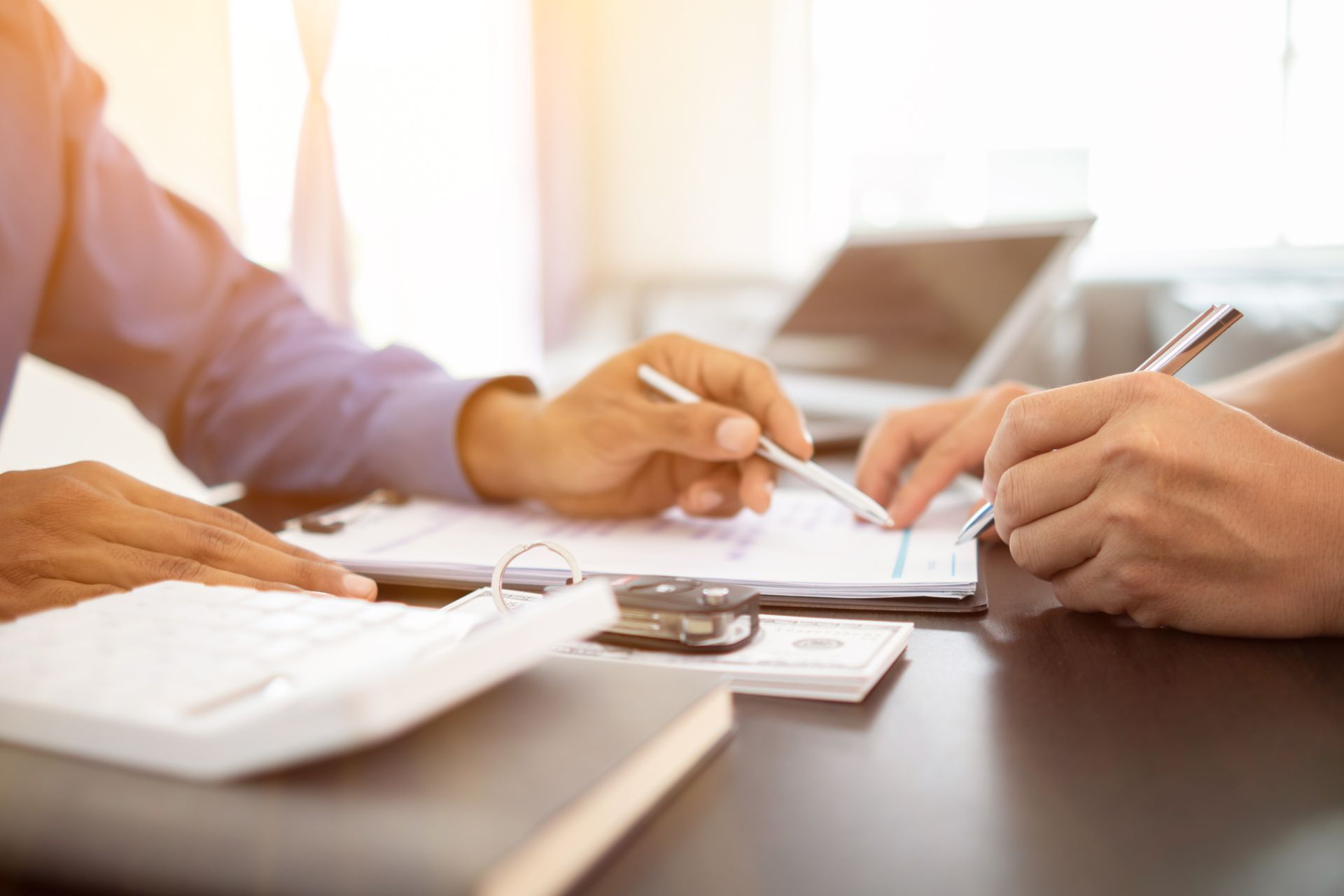 Des mains signant des documents, clés de voiture et calculatrice posées sur la table.