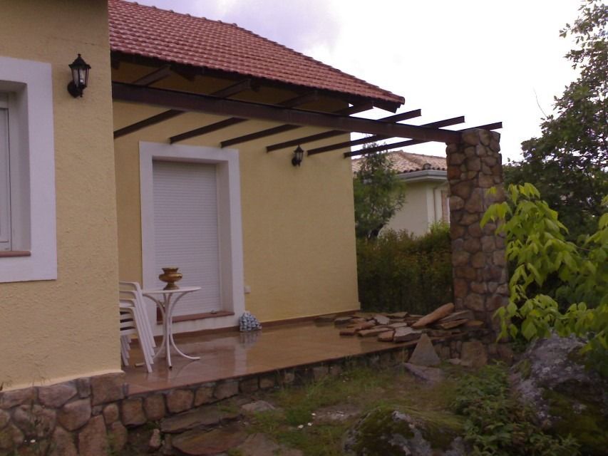 Patio de casa amarilla con silla blanca, techo de tejas y piedras de jardín.