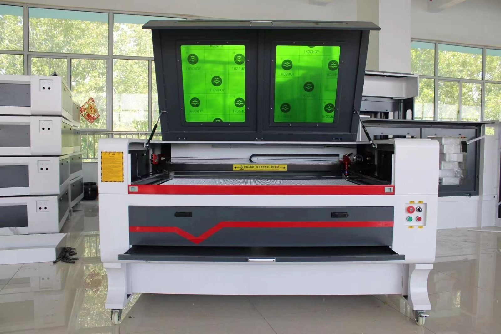 Gran máquina de corte láser industrial con ventanas de visualización verdes en un taller.