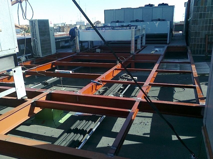 Azotea en construcción con vigas de acero, equipos y conductos bajo un cielo brillante.