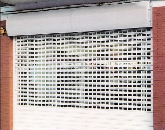 Escaparate de metal blanco cerrado con pequeñas aberturas rectangulares bajo un toldo gris.
