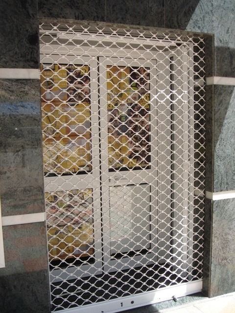Reja de seguridad de metal blanco sobre una puerta con paneles de vidrio esmerilado y cerradura.