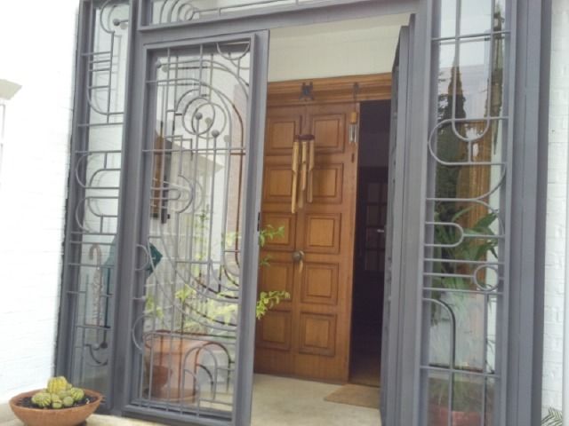 Entrada principal con puerta de madera, verja metálica decorativa y plantas en macetas a ambos lados.