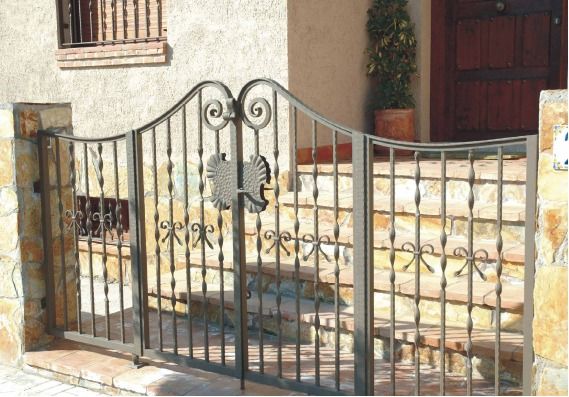 Puerta de hierro forjado negro frente a la entrada de una casa de piedra.