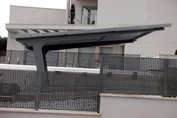 Marquesina moderna sobre un camino de entrada cercado junto a un edificio residencial.