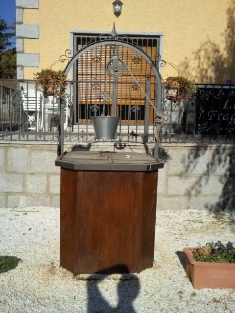 Soporte de exhibición de madera con una jaula de metal y una planta en maceta en un jardín soleado de un patio.