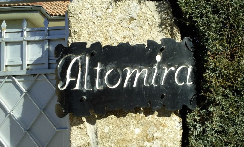 Placa negra con inscripción blanca “Altamira” colocada en un muro de piedra junto a una ventana.