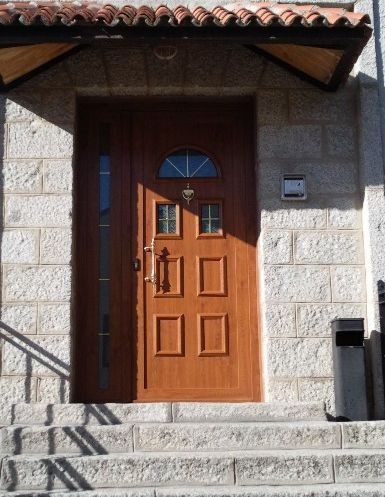 Puerta principal de madera en lo alto de unas escaleras de piedra, enmarcada por un recibidor de estuco y un tejado de tejas.
