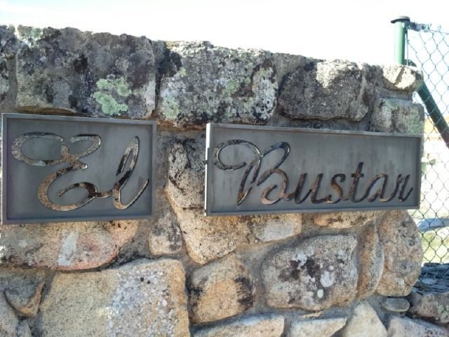 Muro de piedra con dos placas metálicas que dicen “El” y “Burstan” en letra cursiva, junto a una valla verde.