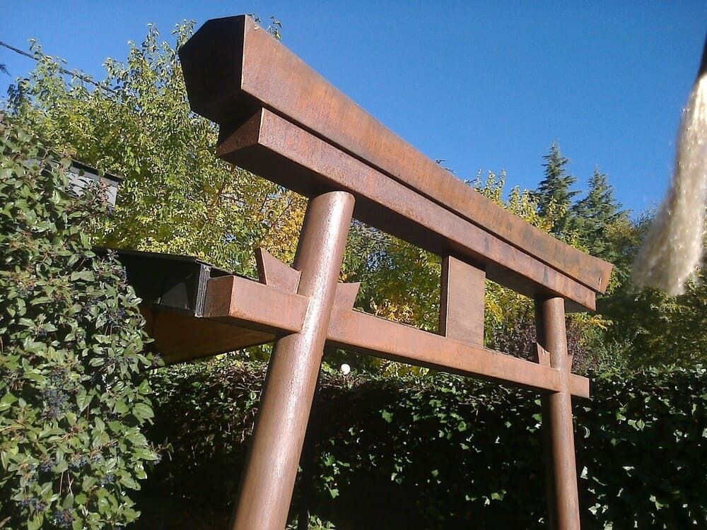 Escultura rústica de puerta torii de madera contra arbustos verdes y cielo azul