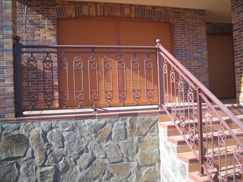 Porche de casa de ladrillo con cimientos de piedra y barandilla de metal, visto junto a los escalones de la entrada.
