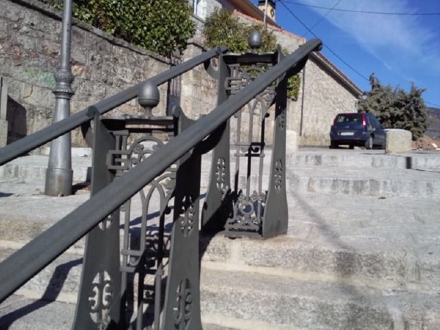 Escaleras de piedra con barandillas de metal negro que conducen a una pendiente exterior junto a un coche aparcado y una casa.