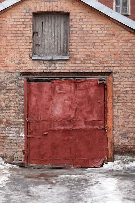 Edificio de ladrillo rojo con una gran puerta de garaje roja y una pequeña ventana tapiada encima.