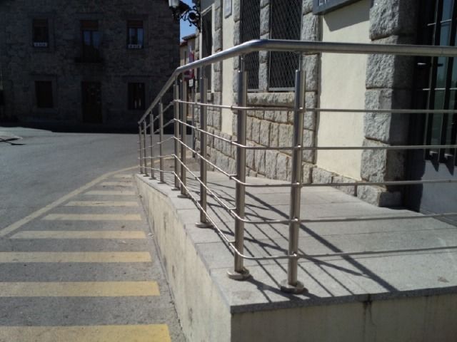 Rampa de hormigón con pasamanos metálicos junto a un paso de peatones señalizado con líneas en una calle soleada.
