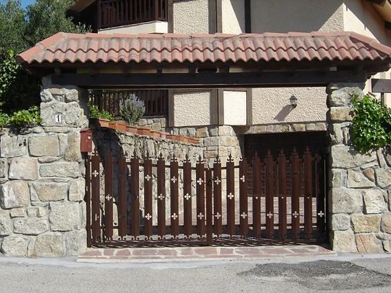 Entrada de piedra a la casa con portón de madera y alero de tejas.