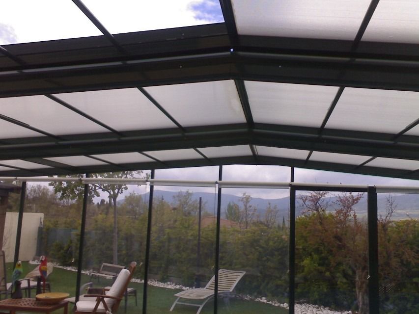 Patio cubierto con techo de metal, tumbonas y vistas a los árboles y las montañas a través de la barandilla de cristal.