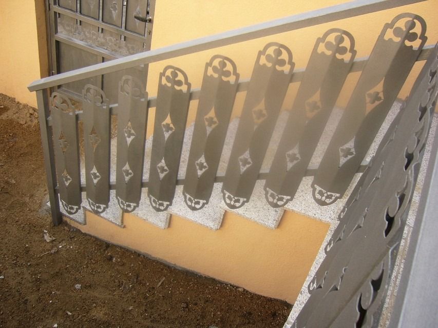 Barandilla metálica de escalera con recortes decorativos en una pared exterior de color beige.