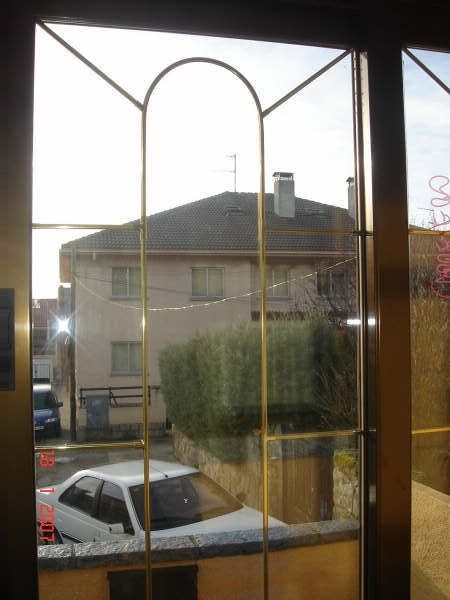 Vista a través de una ventana decorativa de una casa, un coche aparcado y arbustos en una calle residencial.