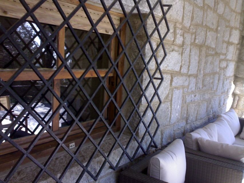 Muro de piedra con ventana enrejada y banco blanco acolchado en un patio.