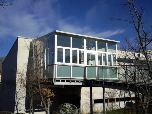 Edificio moderno con grandes ventanales y un balcón con barandilla de cristal contra un cielo azul.