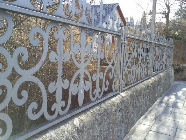 Una valla ornamentada de metal blanco sobre un muro de piedra a lo largo de una calle a plena luz del día.